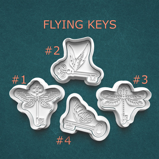 Four metal cookie cutters shaped like keys with butterfly designs on a teal background, labeled with numbers.